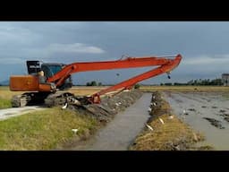 EXCAVATOR LONG ARM HITACHI ZAXIS 120 MAKING A SLOPE ON A SMALL RIVER NEAR PADDY FIELD